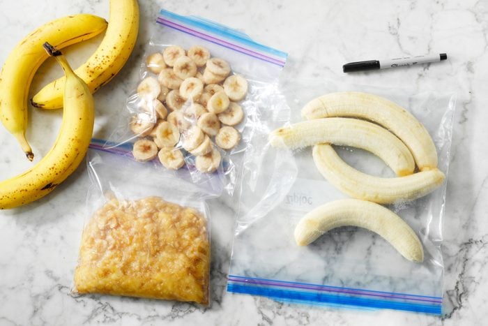 On a marble countertop, fresh bananas next to bags of bananas frozen in three ways: whole, in slices, and mashed