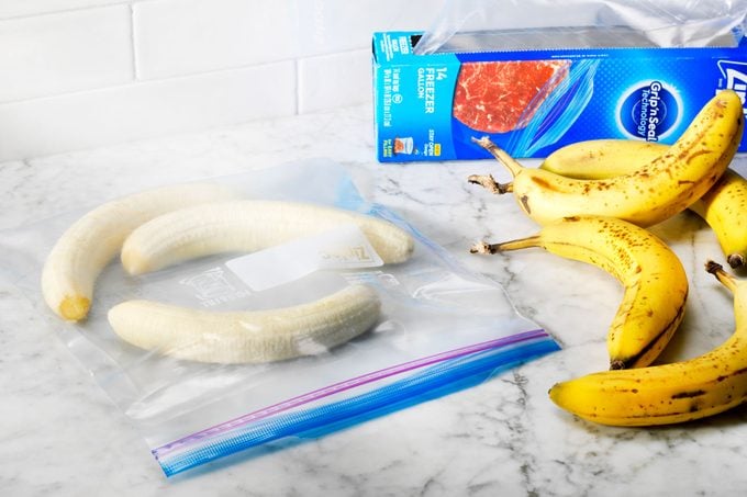 peeled, whole bananas in a freezer bag near fresh, whole bananas and extra freezer bags on a kitchen counter