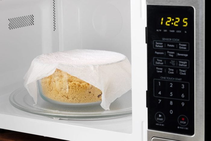 in an open microwave, container of brown sugar in a container with a damp paper towel over top
