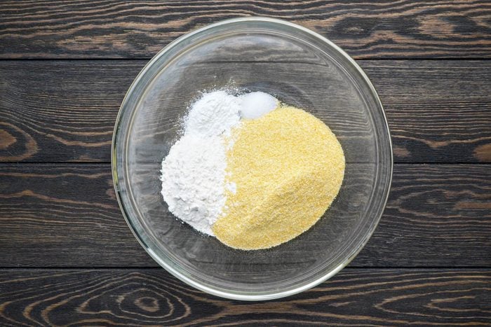 Cornmeal, flour, baking powder mixed in a large bowl, placed on a a wooden table