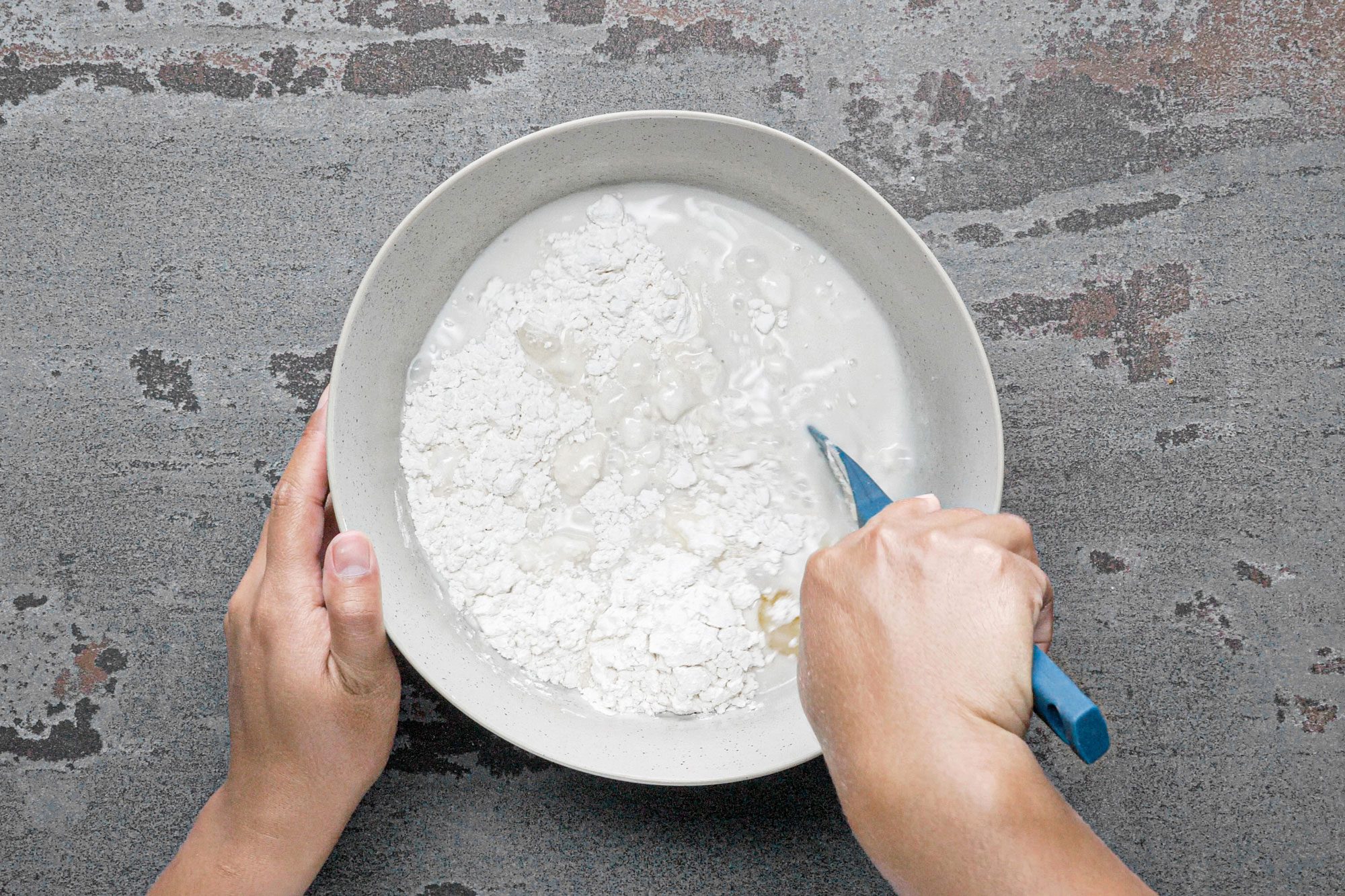 a person mixing flour into milk using spatula in a large bowl