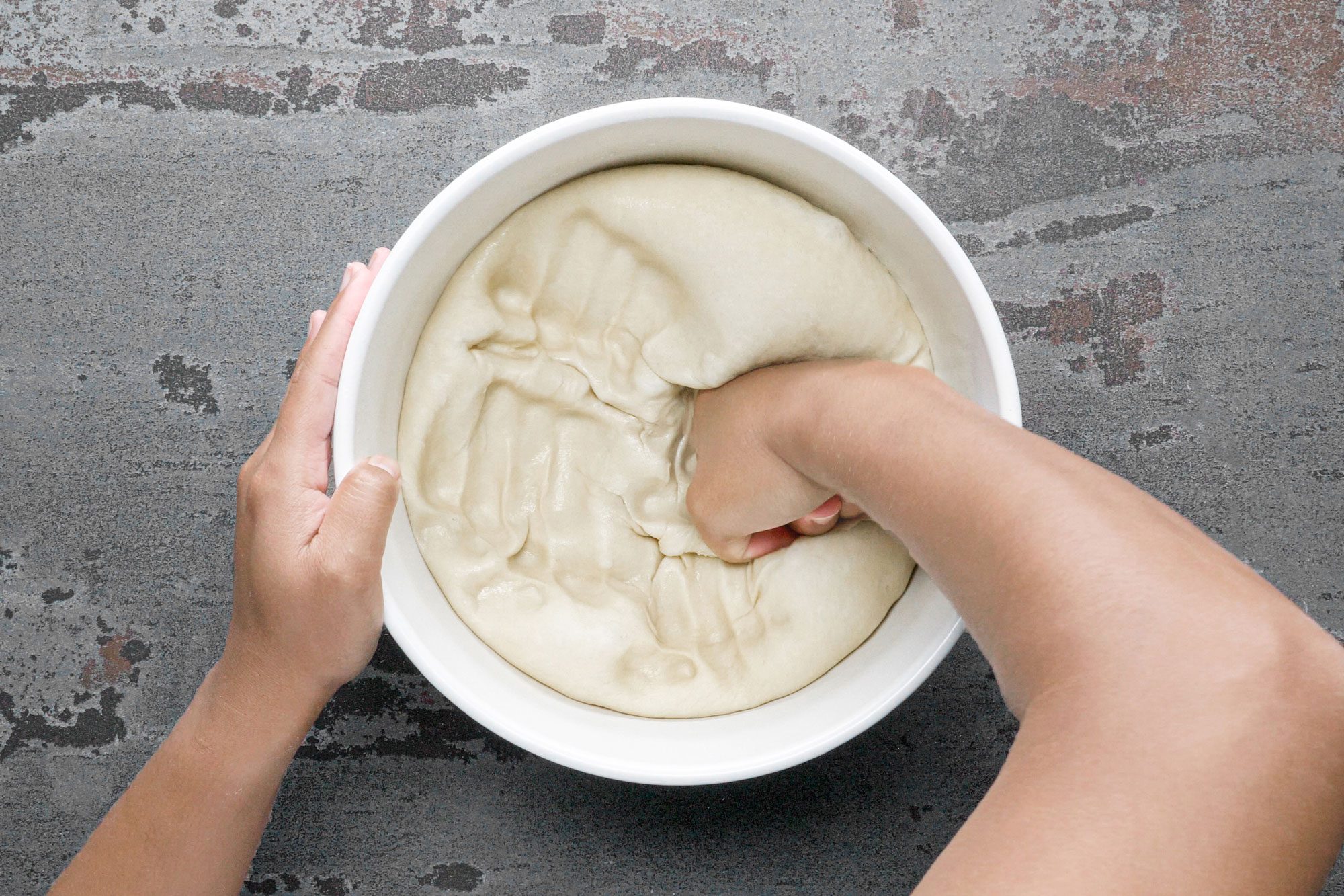 a person kneading dough in a large bowl