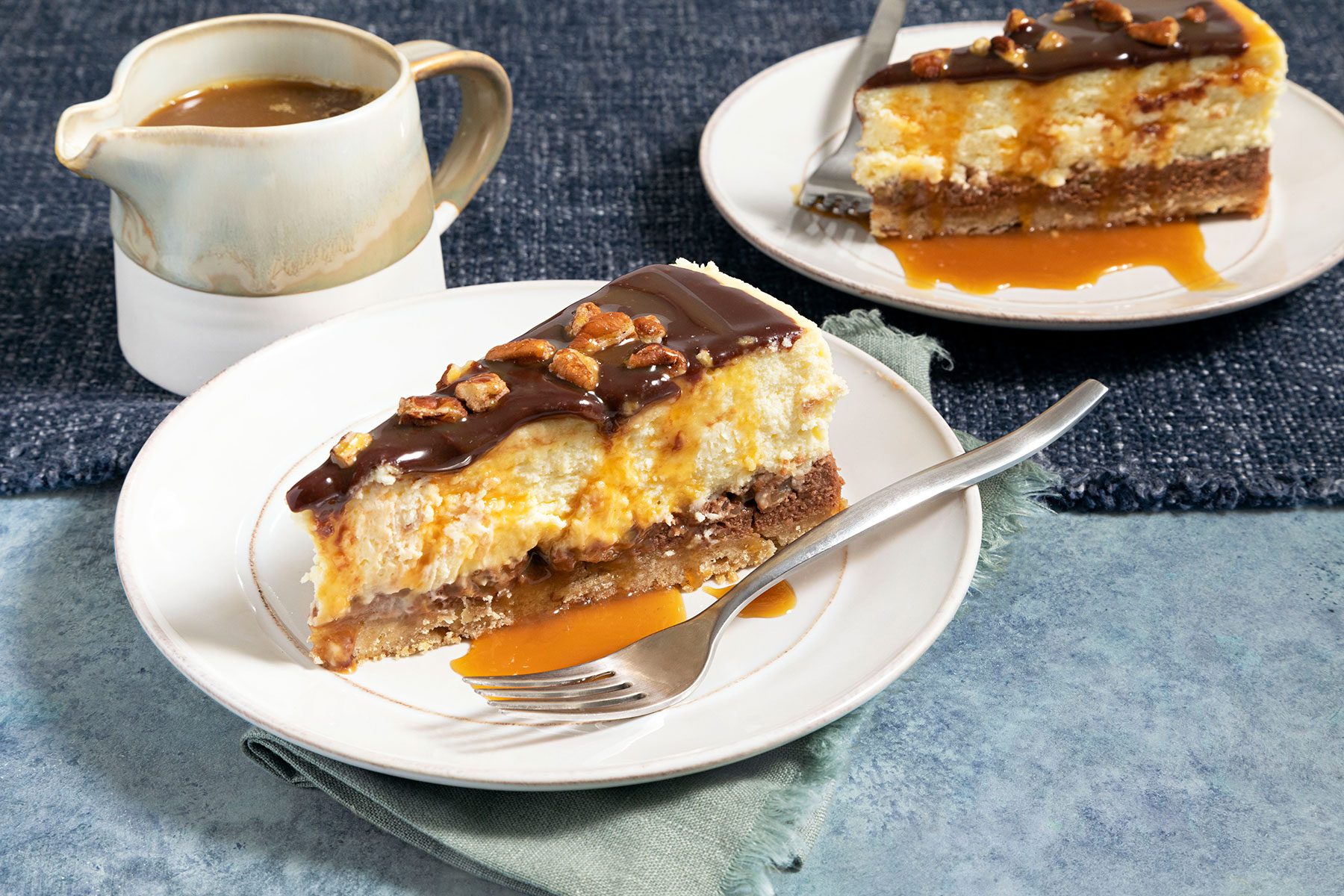 Slices of Layered Turtle Cheesecake served on plates with fork and melted caramel in small pot on side