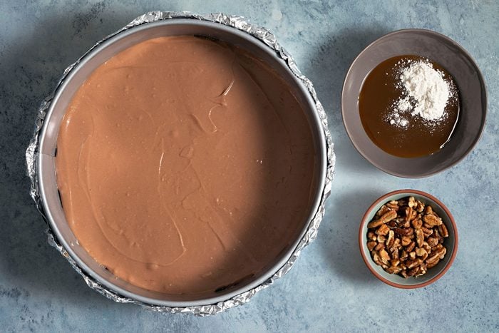 Chocolate covered baking tray and small bowls filled with melted caramel and pecans on the side