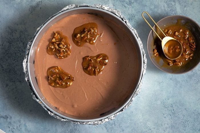 Spoonful of pecans mixed with caramel dropped on melted chocolate mixture in baking tray