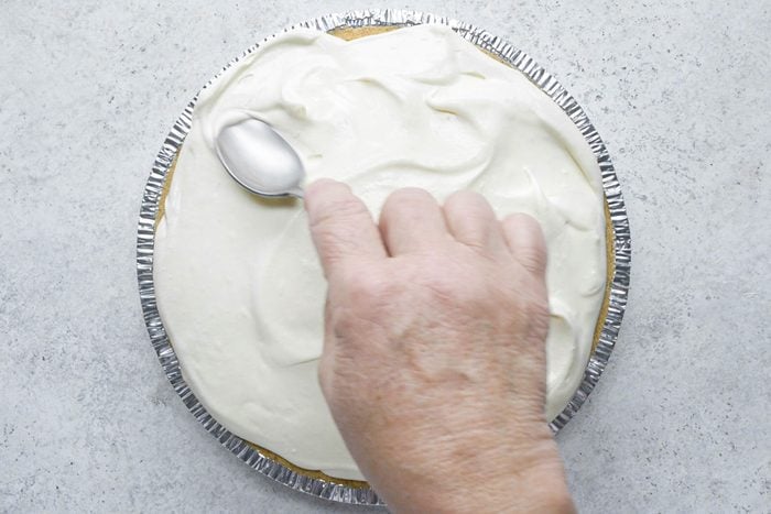a hand smoothing pie filling on pie crust using a spoon