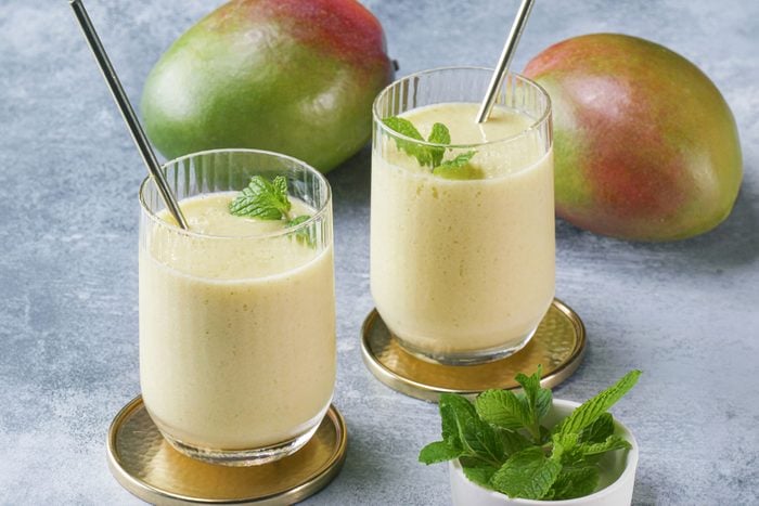 Mango Lassi served in glass with straw and mangoes on the side