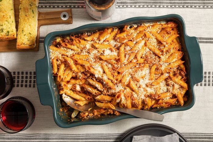 Mostaccioli pasta and bread in a casserole dish on a table with wine on the side