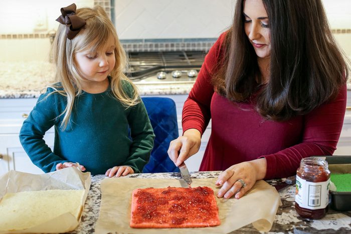 A Mother Spreading Jam on A Large Piece of Bread While Her Daughter Watches