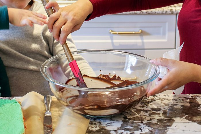 A Person Mixing Chocolate Glaze in a Large Glass Bowl