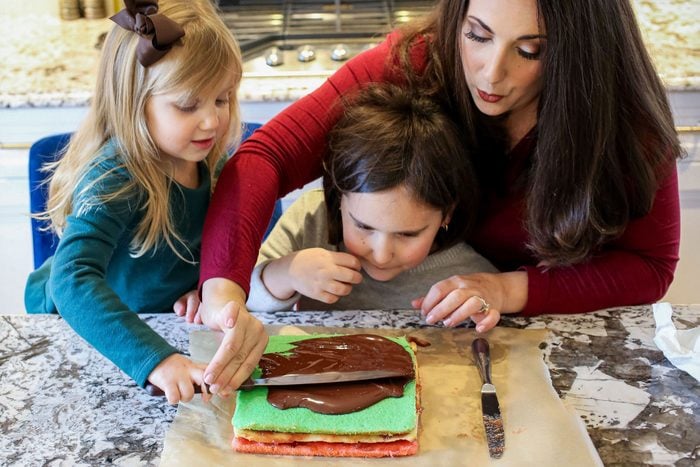 Trio of Daughters and Mother Spreading Chocolate Glaze on Passover Rainbow Cookies Bread/Base