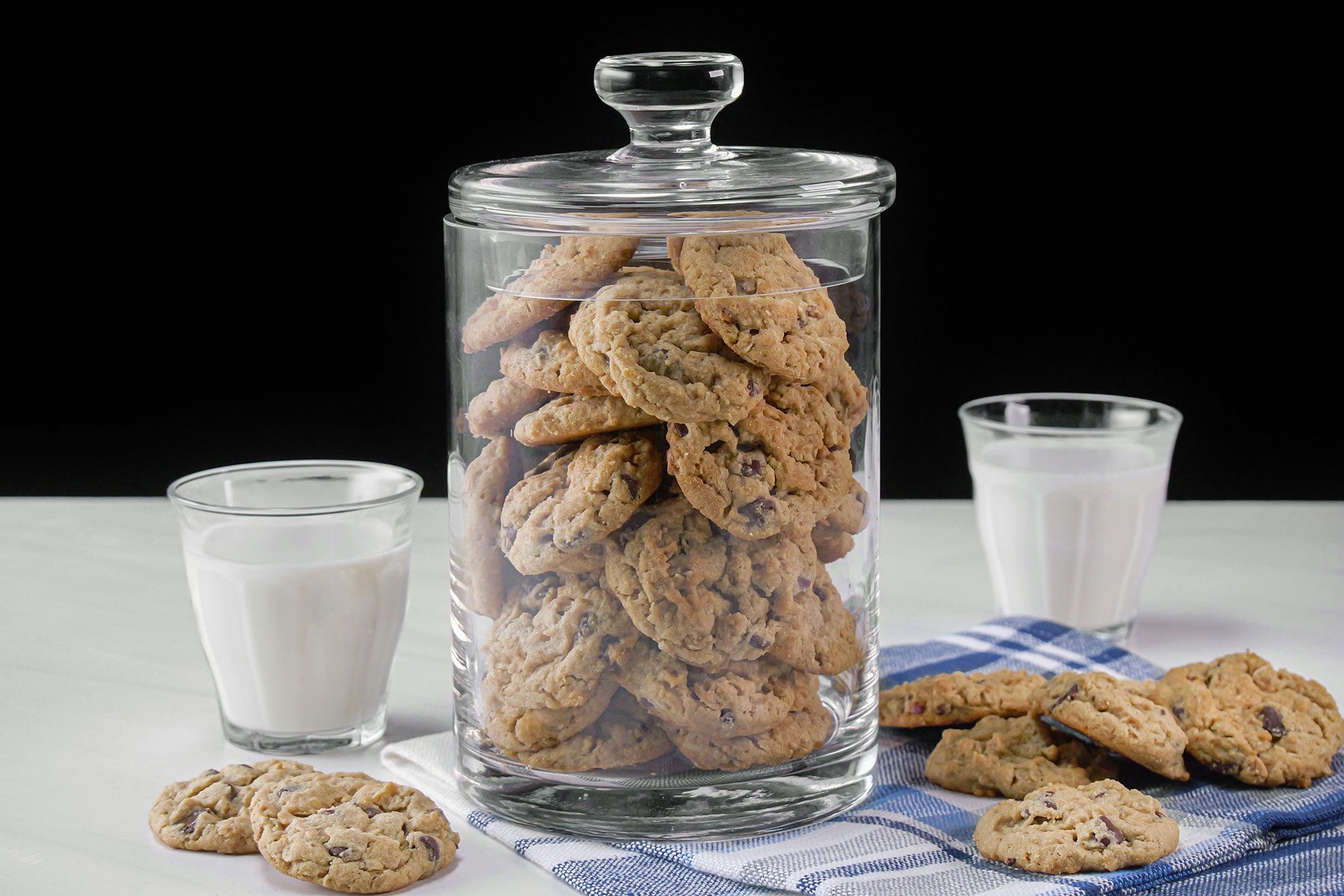 Peanut Butter Chocolate Chip Cookies stored in a glass jar and served on plate with glasses of milk on the side