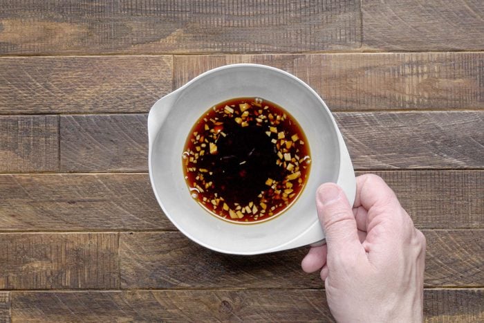 A Hand About to Pick Up a Bowl of Soy Sauce, Wooden Background
