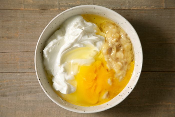 A bowl filled with egg, oil, yogurt, mashed banana and yogurt