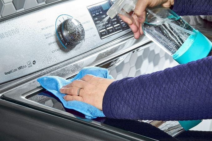 Lady cleaning outer side of washing machine with micro fibre cloth and cleaning spray