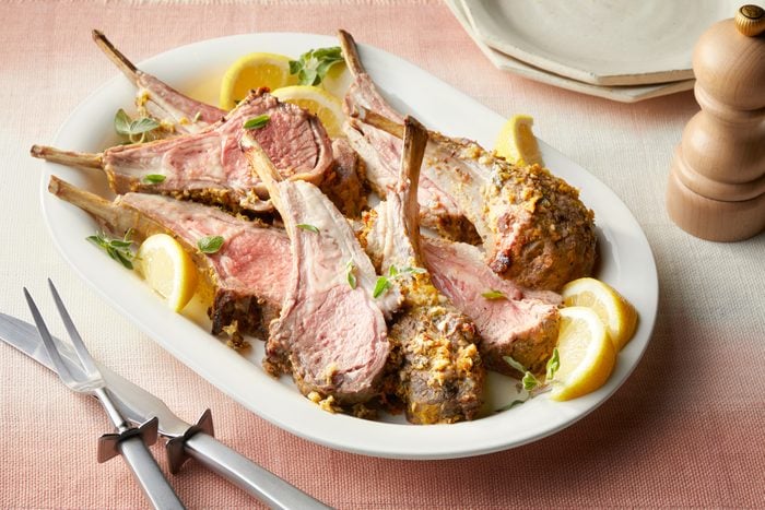 A plate of rack of lamb with lemons and herbs on a table