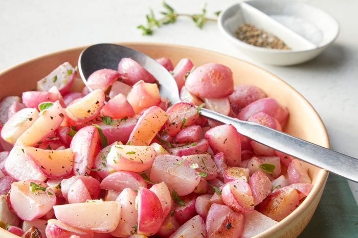 A bowl of roasted radishes with a spoon