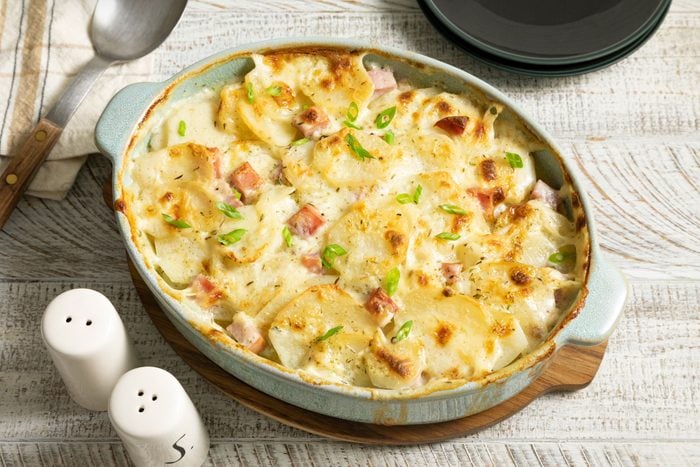 Scalloped Potatoes And Ham in a Baking Dish on a White Painted Wooden Surface