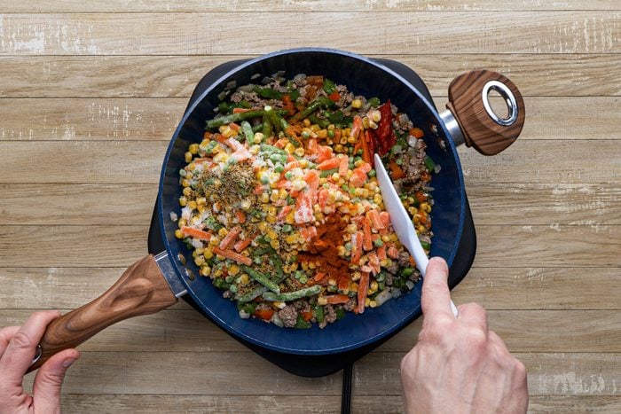 Mixing the vegetables in a large skillet on a wooden surface