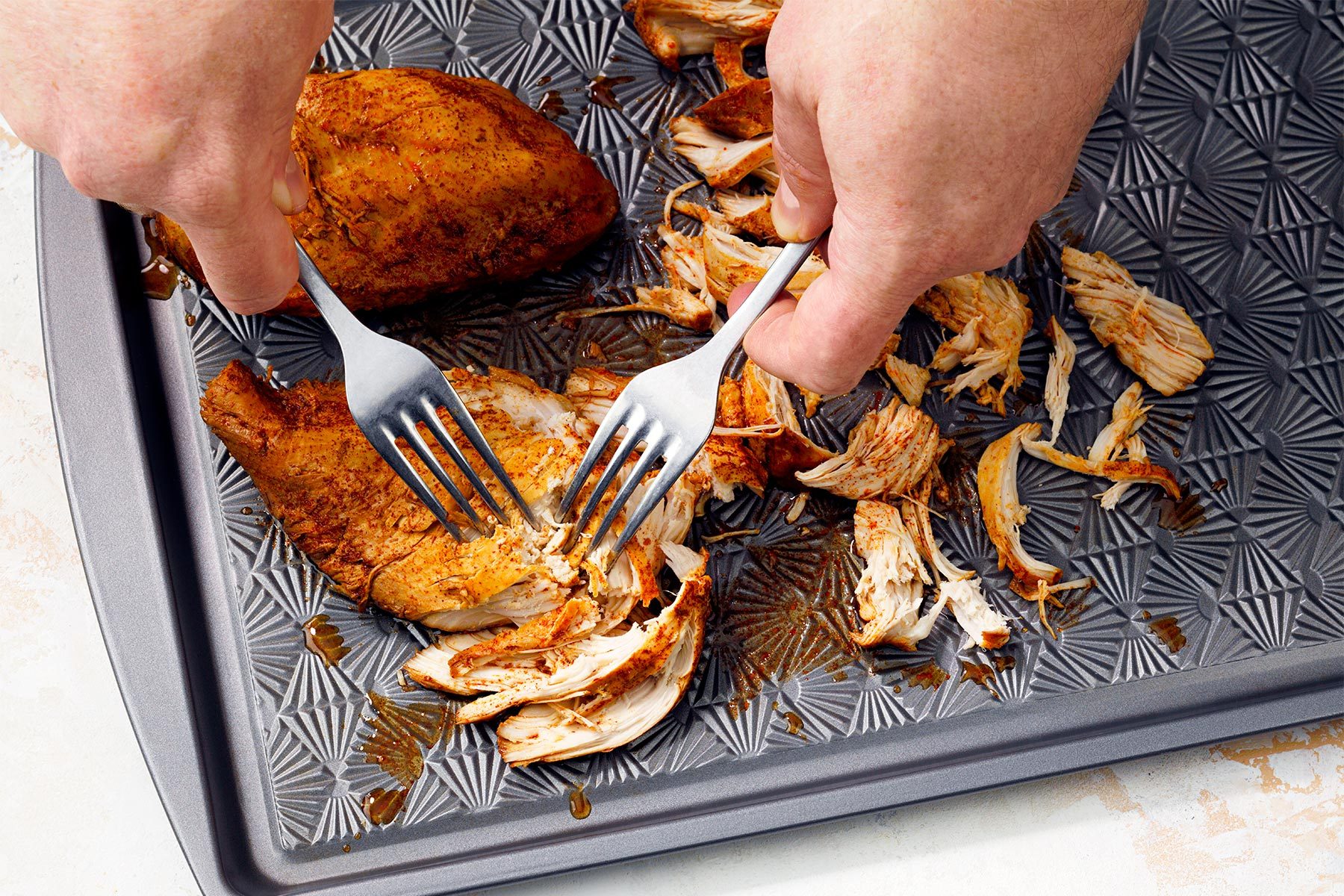 Shredding chicken with forks on baking tray