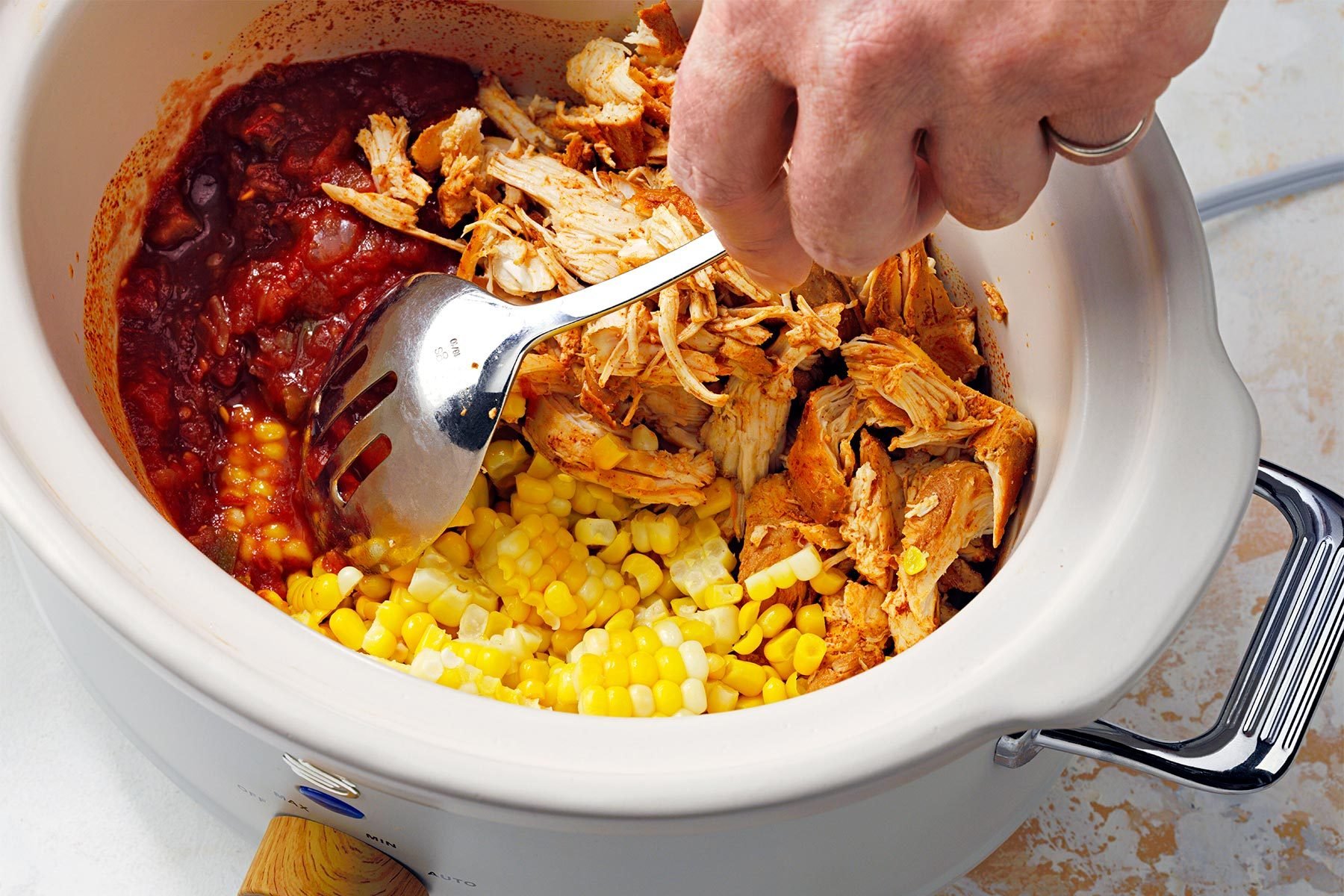 Mixing other ingredients with shredded chicken in slow cooker
