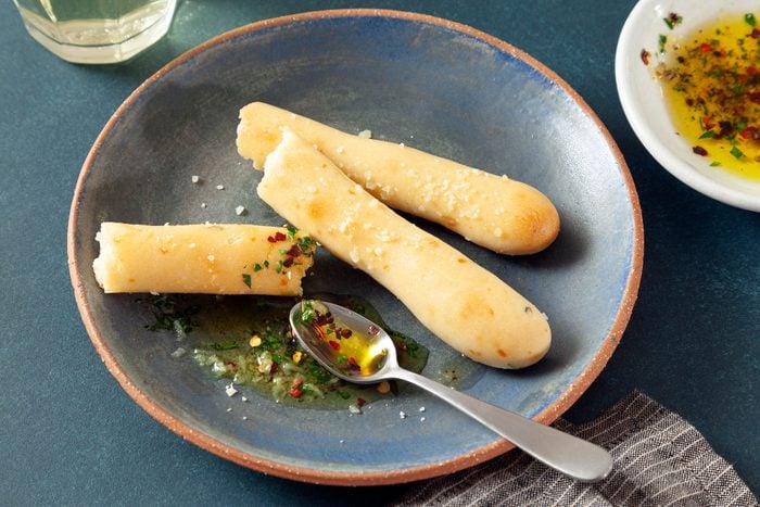 Soft Garlic Breadsticks Served in a Terracotta Plate with Spoon on Teal Surface