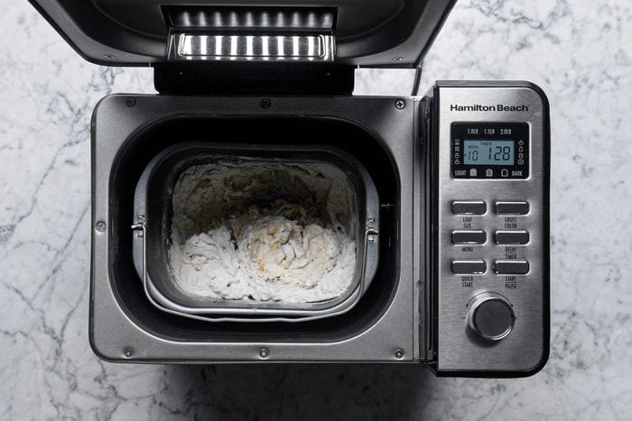 preparing dough in a bread maker machine on marble surface