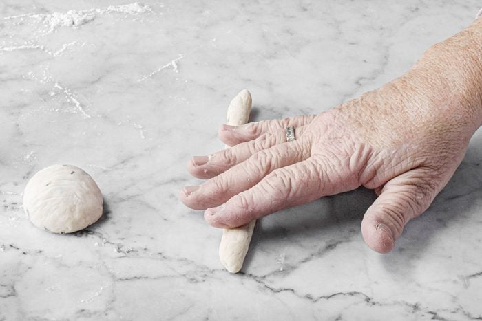 a person rolling dough into a rope shape on a marble surface to make Breadsticks