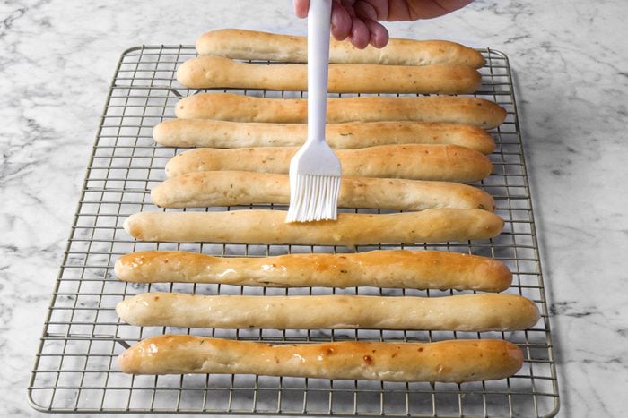 Brushing Butter on Soft Garlic Breadsticks Placed on Wire Rack on Marble Surface