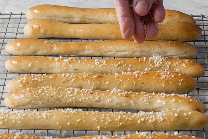 Garnishing Soft Garlic Breadsticks by Sprinkling Grated Parmesan Cheese on it