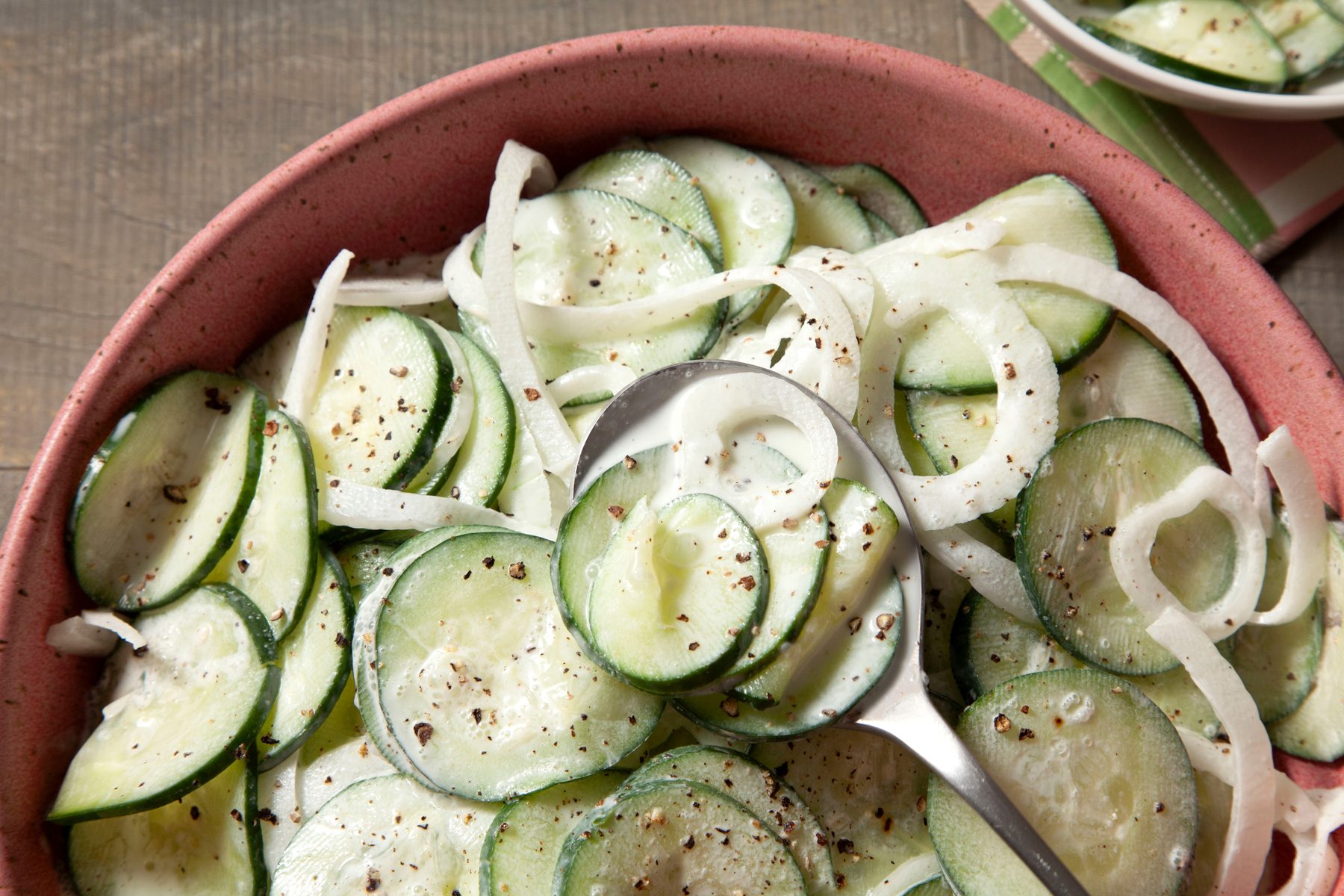 A bowl of sour cream cucumbers with a spoon