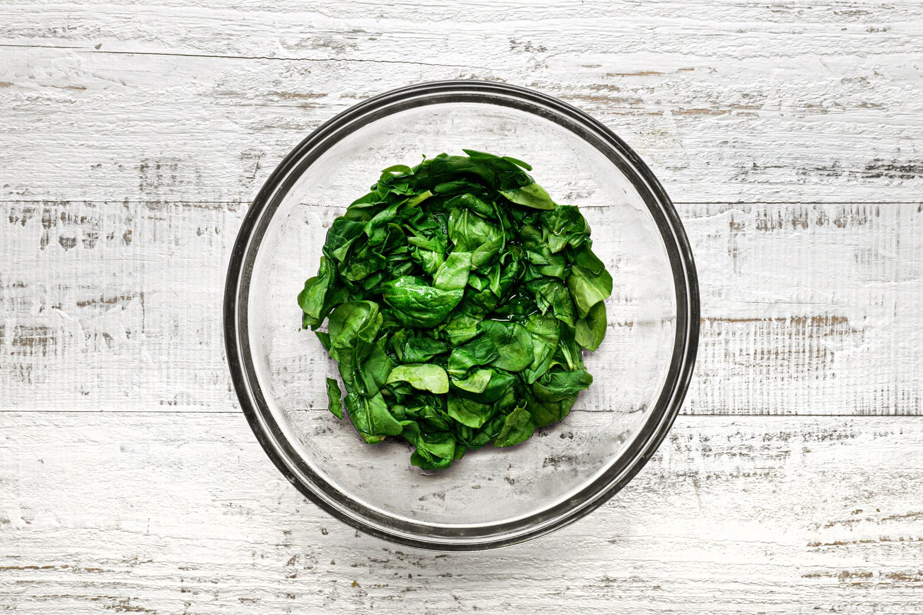 A bowl of wilted spinach over a wooden table.