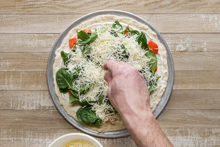 Layering the pizza with vegetables spinach and cheese 