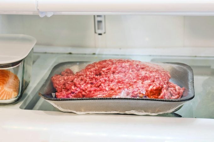 raw ground beef unthawing in a fridge in the original grocery store package