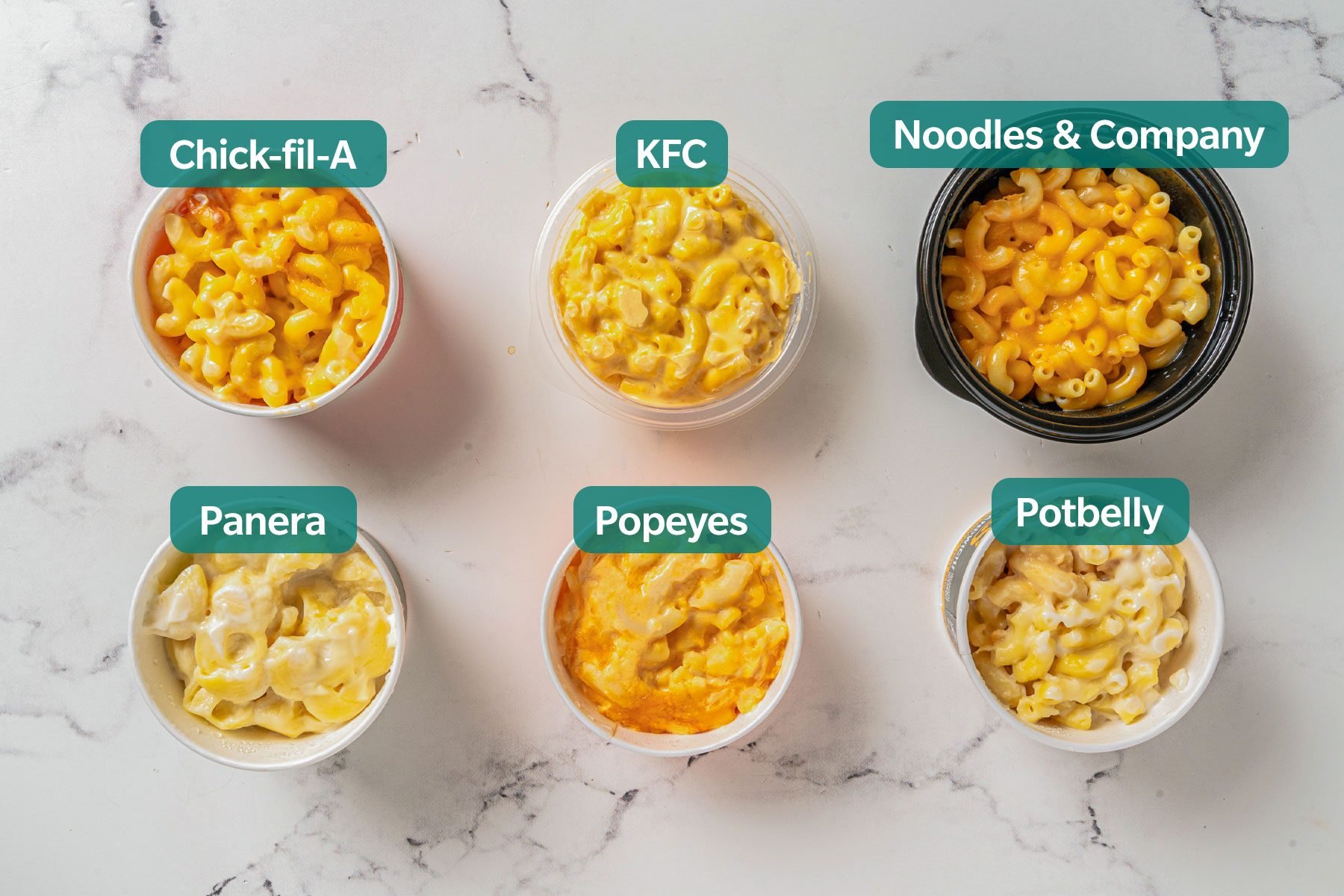 6 cups of mac and cheese from different fast food brands on a marble surface