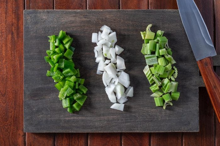 Chopped Green Bell Peppers, white onions and Celery on a wooden chopping board with knife