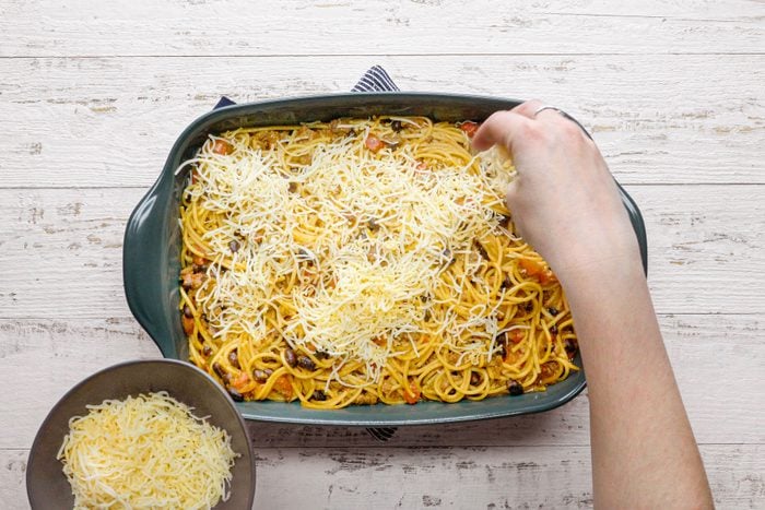 Sprinkling cheese on Taco Spaghetti in a baking pan