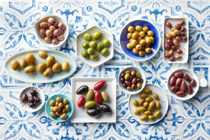 many types of olives in different dishes arranged on a Mediterranean blue tile background