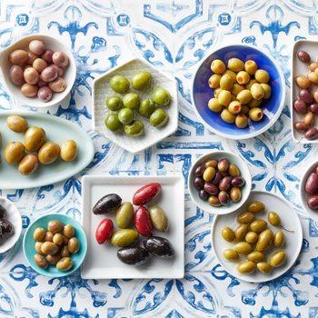 many types of olives in different dishes arranged on a Mediterranean blue tile background