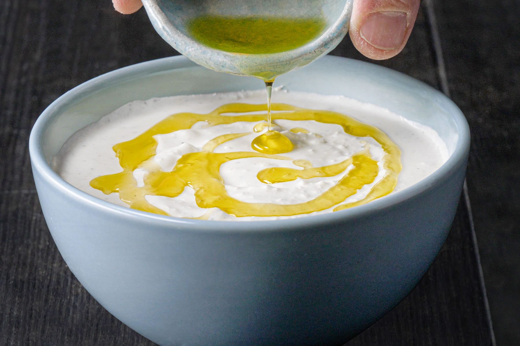 Drizzling oil over the Whipped Feta Dip in a small bowl