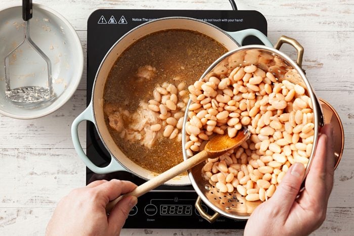Beans being added in a broth to cook White Chicken Chili