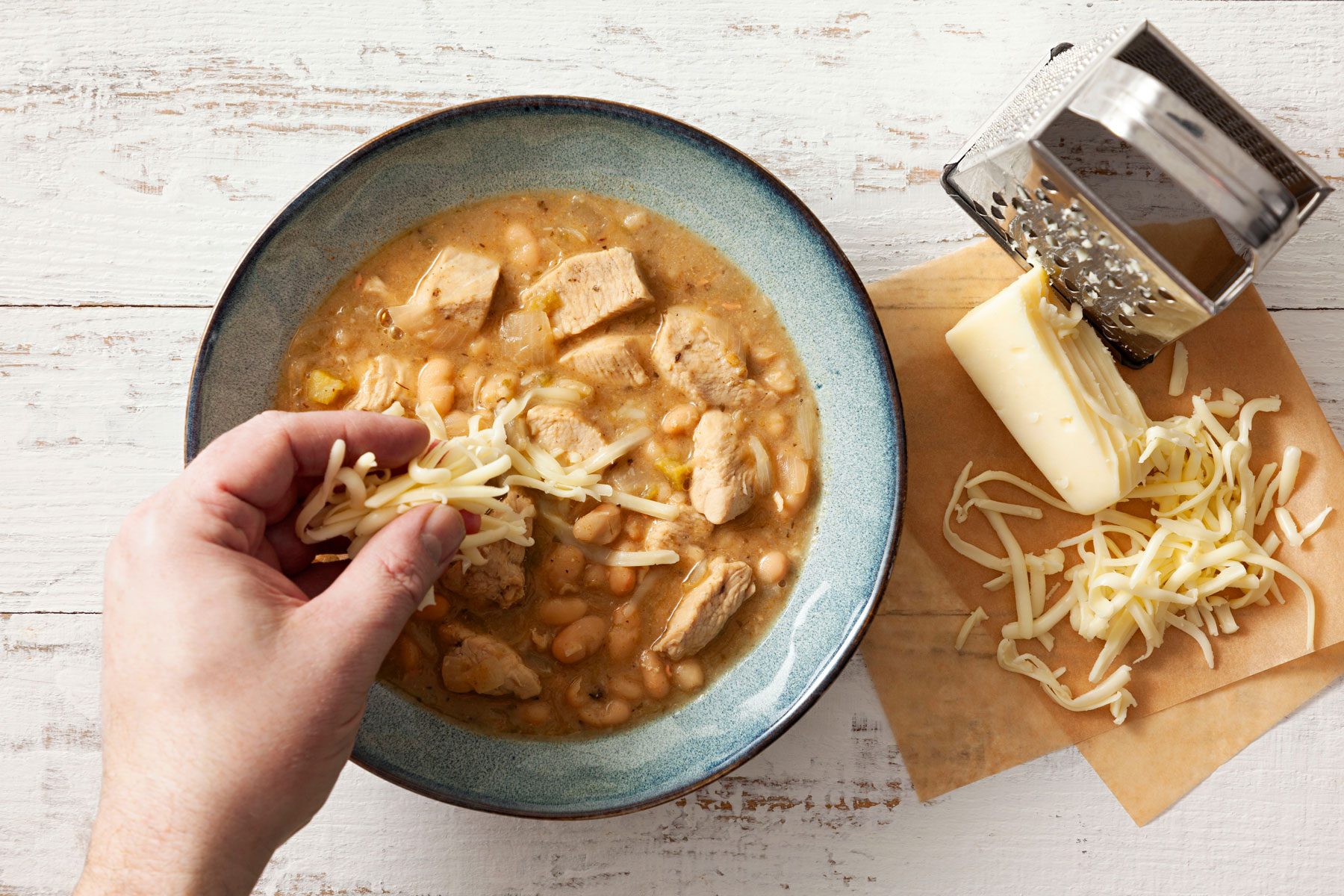 Adding cheese on White-Chicken-Chili in a bowl on a wooden surface