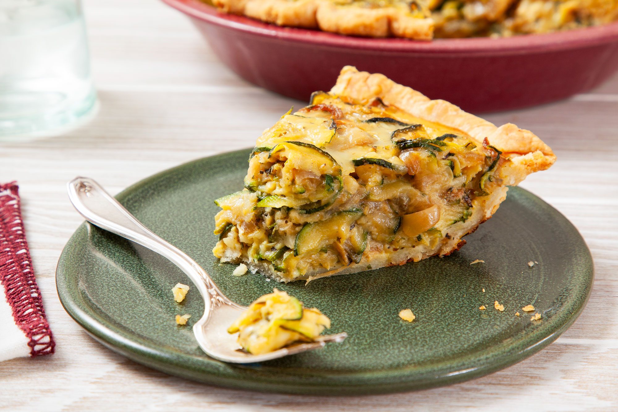 A Slice of Zucchini Quiche with Fork on a Green Ceramic Plate on Wooden Surface