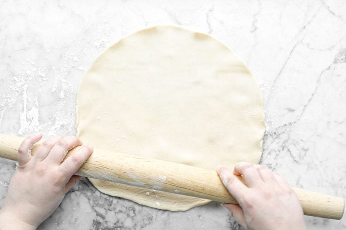 Hands Rolling Dough with Wooden Rolling Pin on Marble Surface