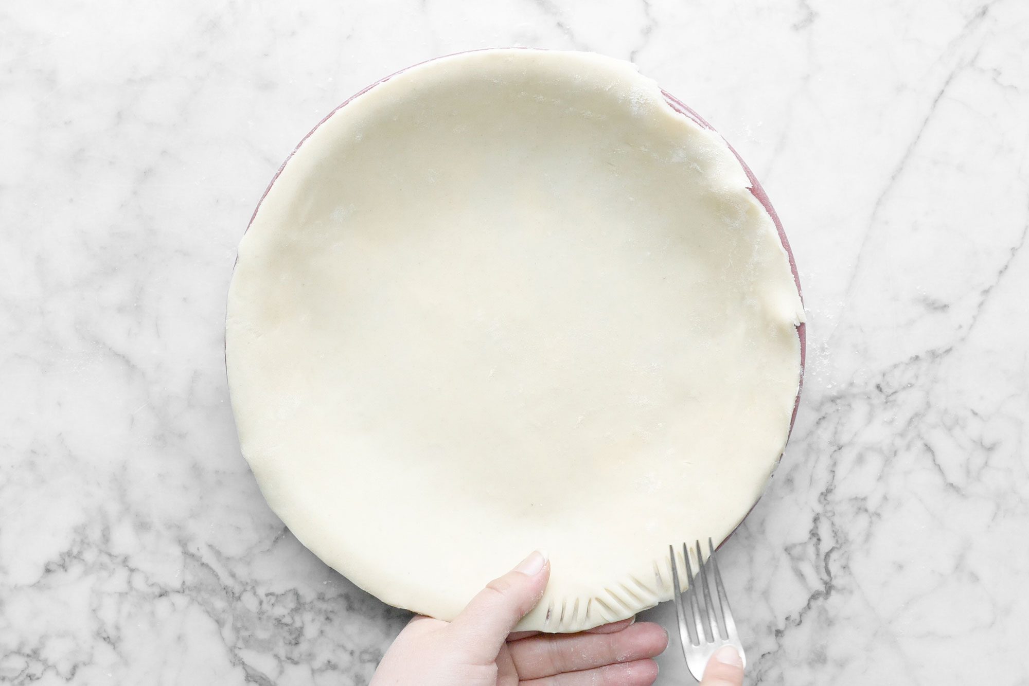 Pressing Rolled Dough Sides on Pie Plate with Fork on Marble Surface
