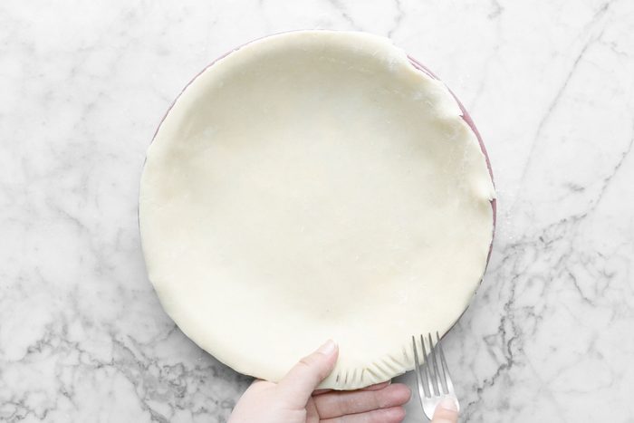 Pressing Rolled Dough Sides on Pie Plate with Fork on Marble Surface