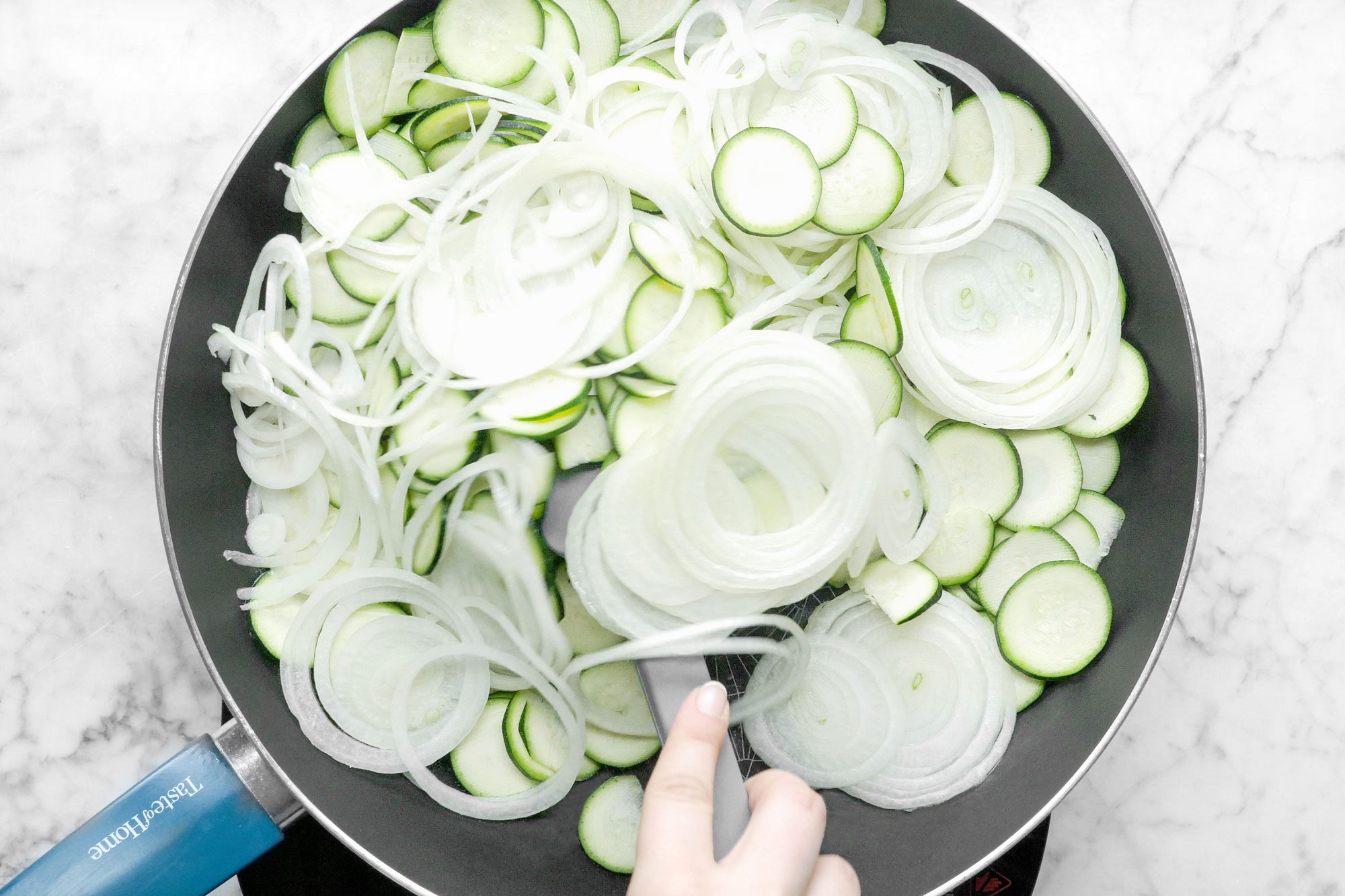 Cooking Zucchini and Onion in A Non Stick Skillet , Marble Background
