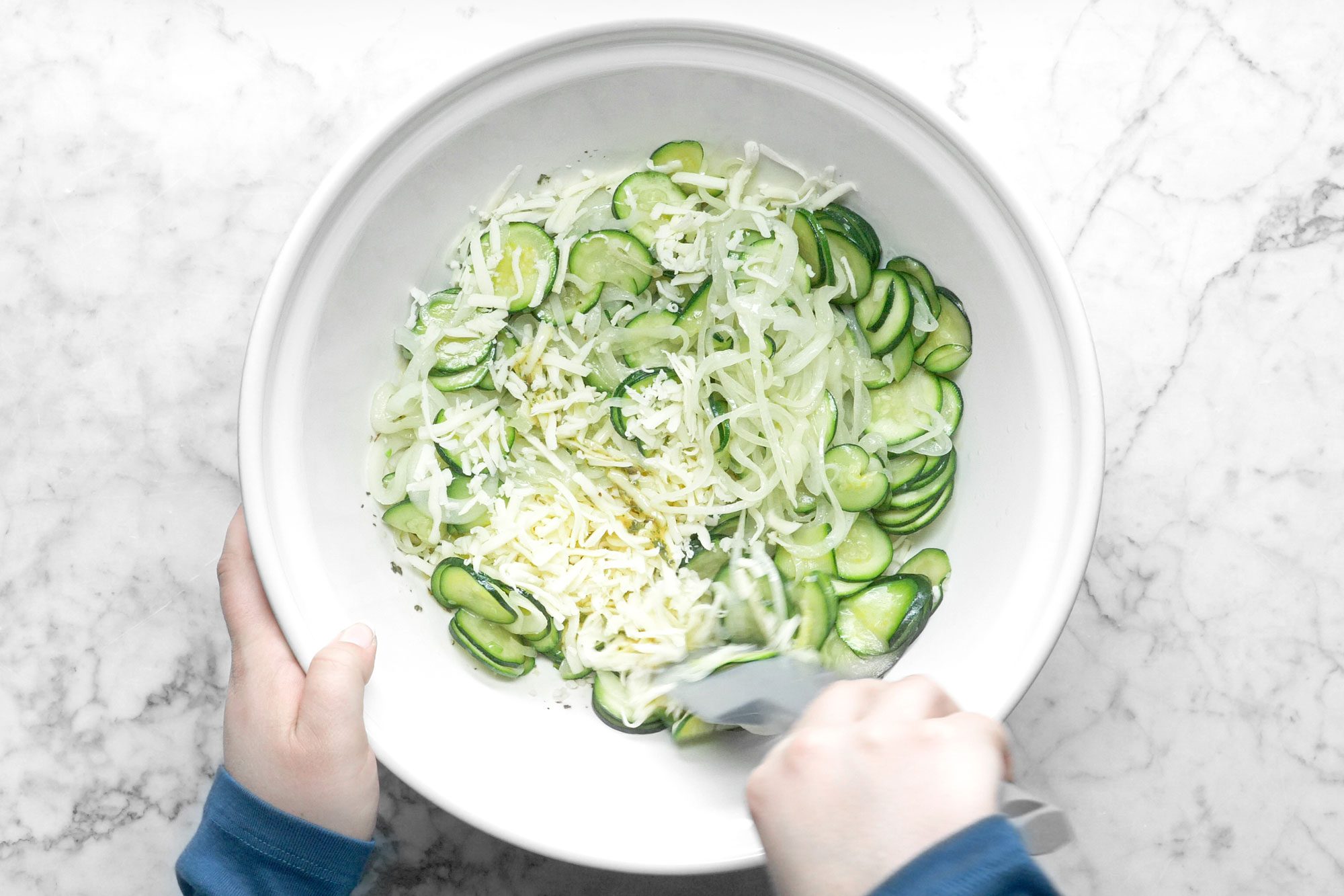 Mixing Zucchini and Cheese in a large white ceramic bowl on marble surface