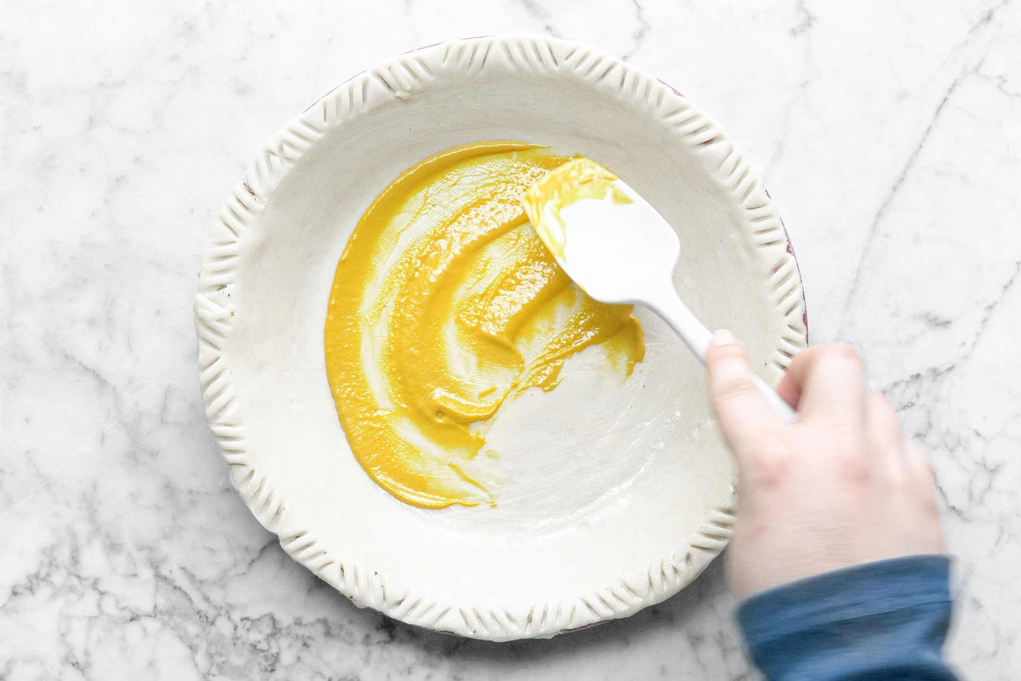 spreading mustard on the Zucchini Quiche Base, marble background