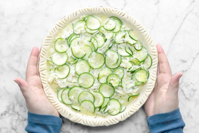 Zucchini Quiche In a Pie Plate Held in Hands, Marble Background.